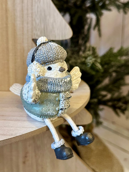 A small Mr Christmas Bird tree decoration, wearing a knitted hat, scarf and boots, sits on a wooden surface with greenery in the background, perfect for festive Christmas décor.