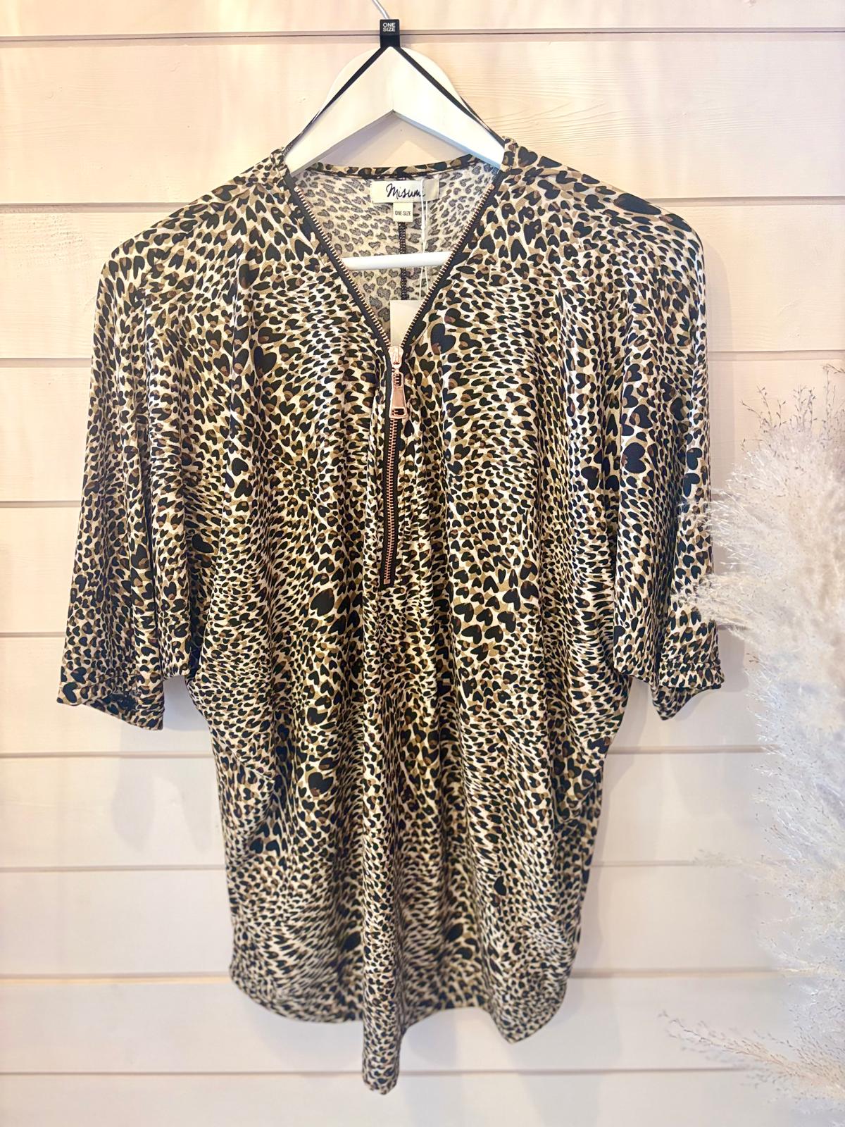 Leopard-print blouse with a front zip, shown on a hanger against a light-coloured wooden plank wall background.