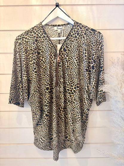 Leopard-print blouse with a front zip, shown on a hanger against a light-coloured wooden plank wall background.