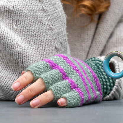 A person wearing a grey jumper and fingerless gloves made from a recycled blend with green and purple stripes rests their hand on a surface.