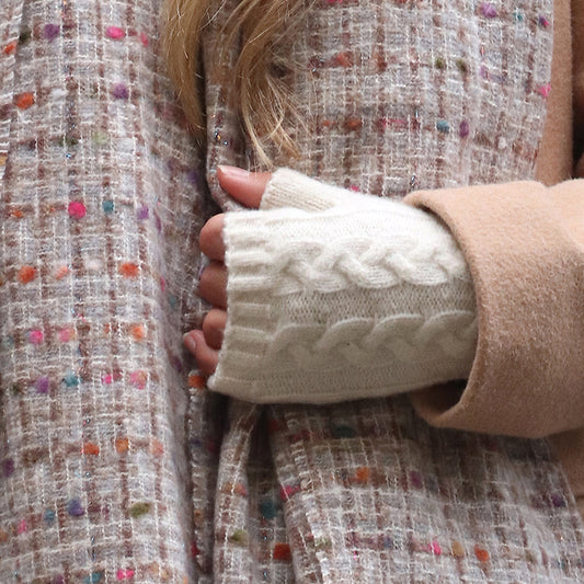 A person in a beige coat and cream vegan-friendly wrist warmers, their hand resting on a textured, multicoloured patterned fabric.