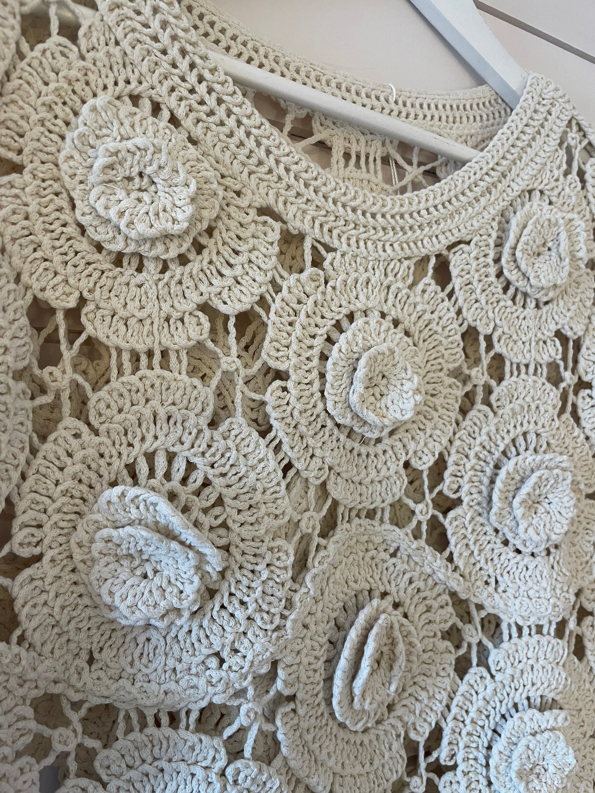 Close-up of a cream floral jumper, perfect for spring with large, circular flower motifs and intricate openwork detailing—an ideal sheer layering piece.
