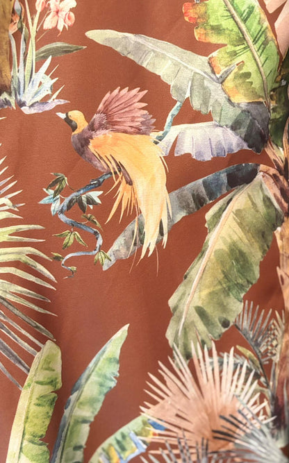 Illustration of a yellow and brown bird perched on a branch, surrounded by green tropical leaves and flowers, capturing the lively essence of a Jungle Jumpsuit Dress against a brown background.