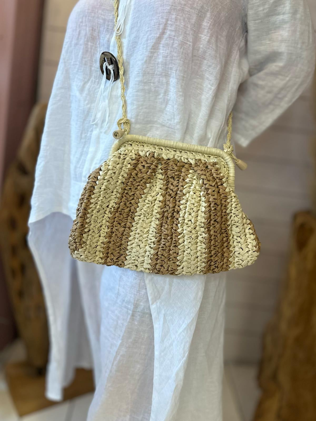 A person wearing a white linen outfit carries a small, two-toned straw bag with a gold clasp—an environmentally friendly, vegan-friendly accessory.