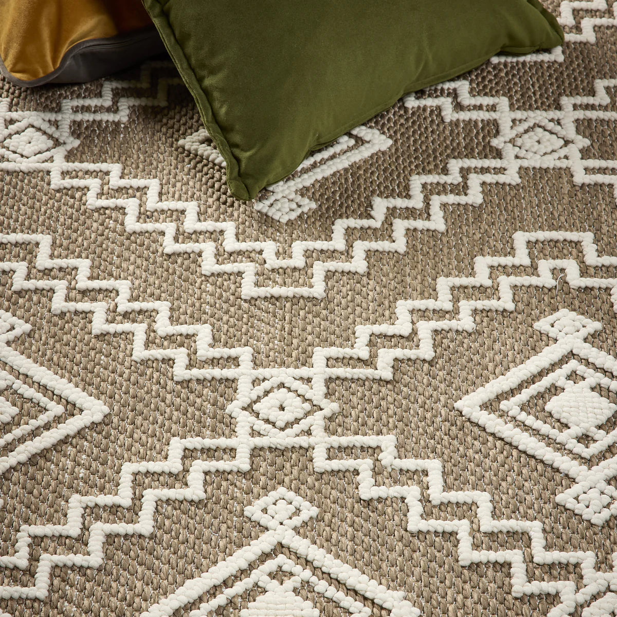Green cushion sits on a contemporary-style rug, the Diamond Coffee Rug, which features a geometric white pattern of zigzags and diamond shapes on a hard-wearing beige background.