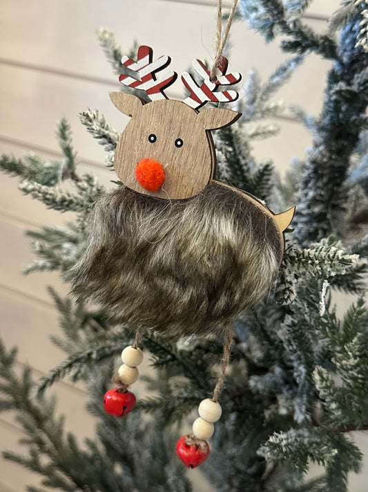 A fluffy hanging reindeer ornament with faux fur, a red nose, and beaded legs adds charm to your festive décor, suspended on a snow-dusted Christmas tree.