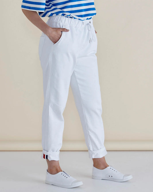 Person dressed in snow-white jeans, a blue and white striped top, and white trainers, standing with hands in pockets against a neutral background—a nod to sustainable fashion.