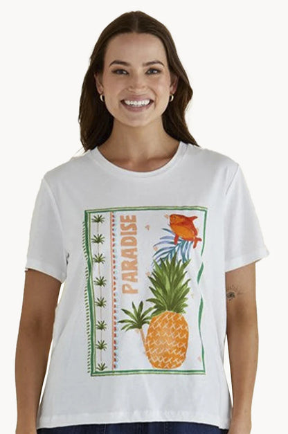 A woman wearing a white T-shirt with a graphic of a pineapple, fish, green plants and the word PARADISE printed vertically, made from breathable fabric for relaxed coastal style.