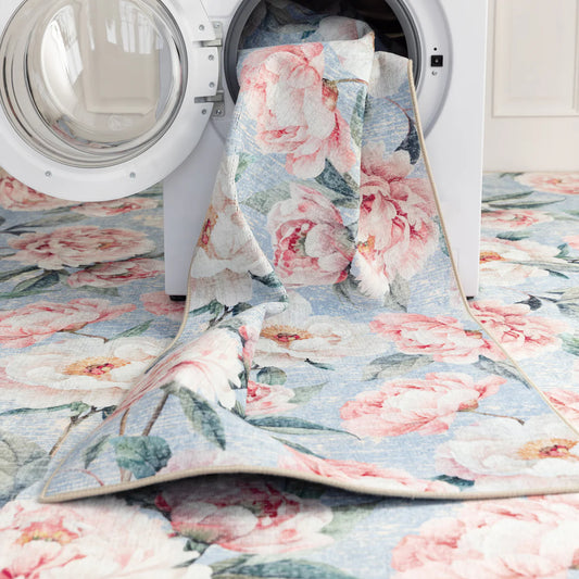 The floral-patterned quilt, reminiscent of blooming peonies, is partially inside a front-loading washing machine, harmoniously matching the floral floor covering.