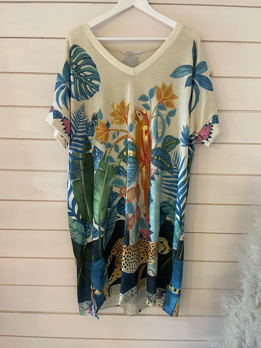 Beige oversized maxi dress featuring a colourful tropical animal print—leaves, parrot, and cheetah—hanging on a white hanger against a pale wooden wall.