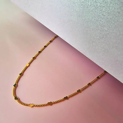 A heart-shaped necklace with gold chain links rests on a pink surface, partly covered by a white sheet—ideal as a stylish and hypoallergenic accessory for everyday wear.