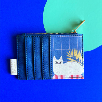 A blue cat purse with a zip, featuring a white cat illustration, a plant, and a grid pattern on a vibrant background—a quirky accessory that's ideal as a gift for cat lovers.