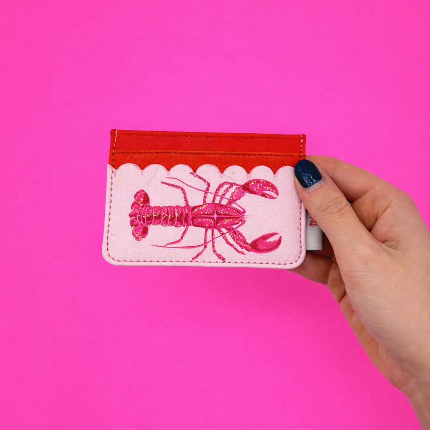 A hand holds a small Coral Lobster Card Holder, made from sturdy PVC with card slots and a glossy lobster illustration, set against a vibrant pink background.