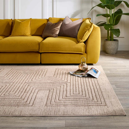 A mustard yellow sofa with assorted cushions rests on a Calacatta Lines Natural Rug; a plant, teapot and magazines are close by on the light-coloured wooden floor.