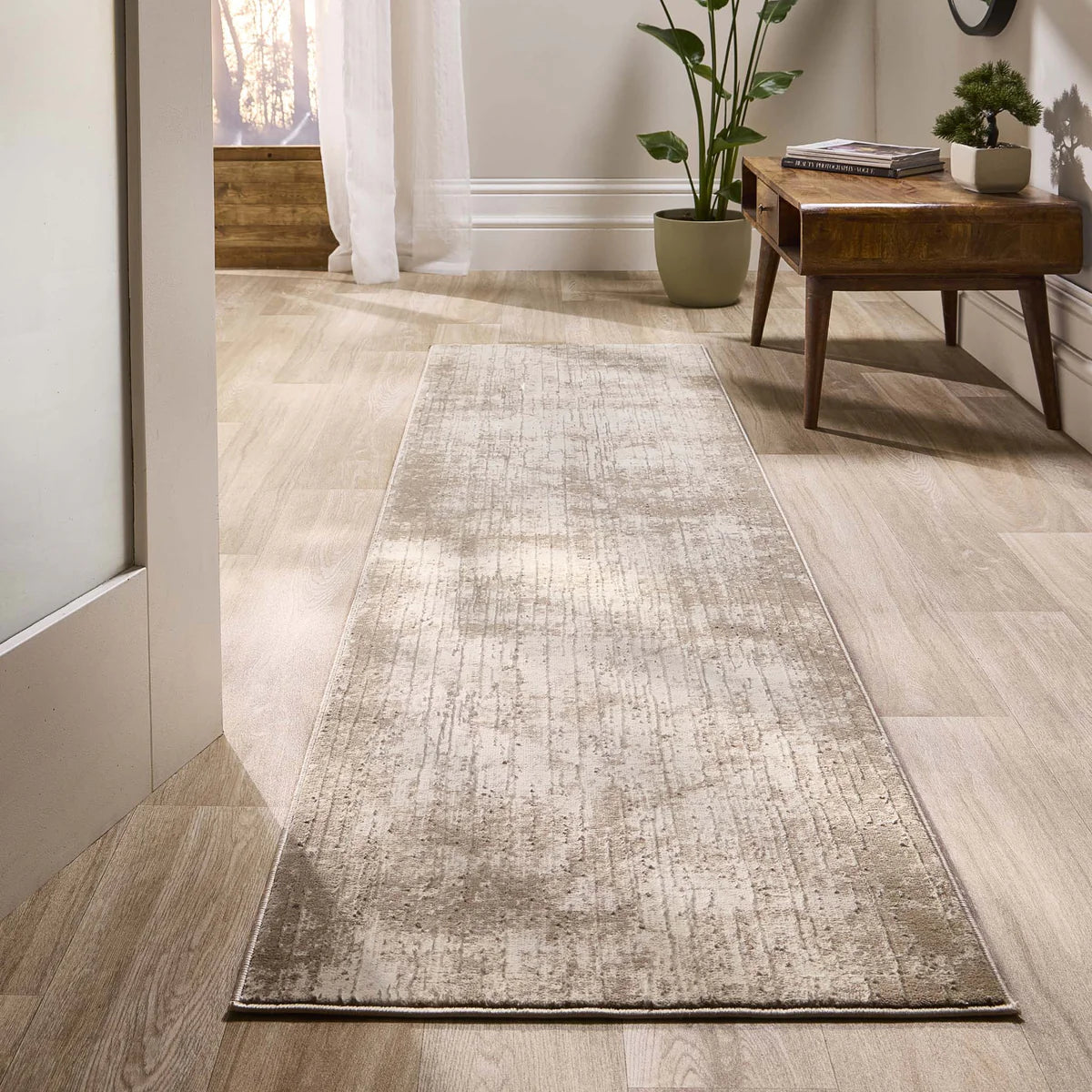 A contemporary beige vegan rug with a subtle textured pattern rests on a light wooden floor in a hallway, beside a wooden bench adorned with potted plants.