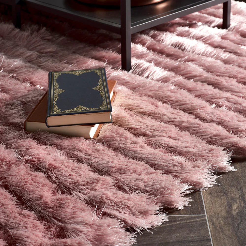 A close-up of a soft-pile pink rug with two books resting on top, beside a metal table leg on a dark wooden floor.