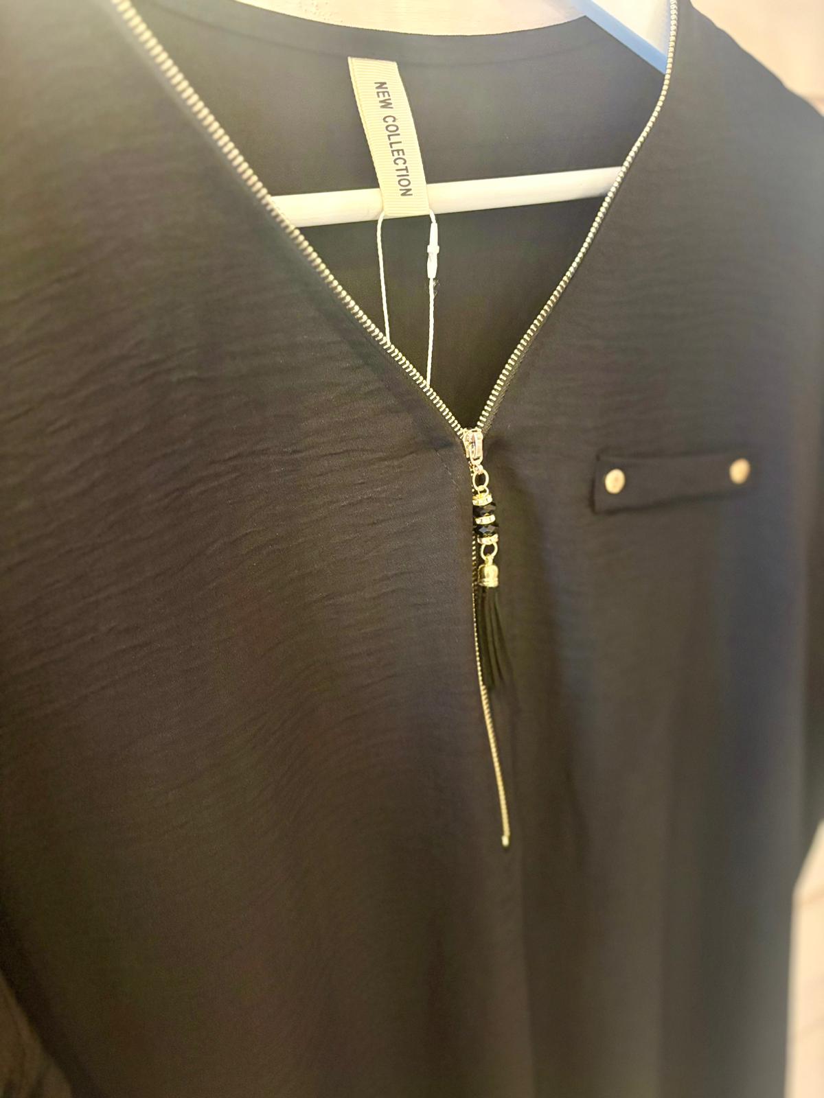 Close-up of a black garment on a hanger, featuring a V-neck with a silver zip and a decorative buttoned tab on the chest.