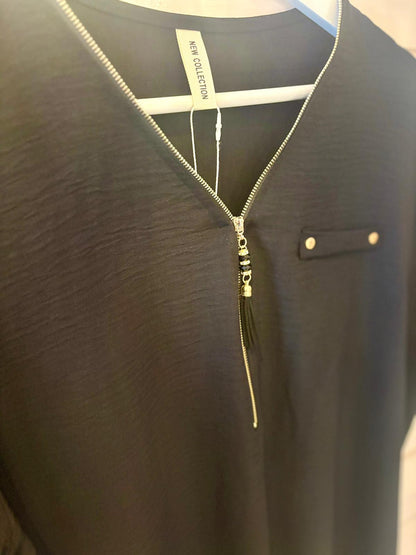 Close-up of a black garment on a hanger, featuring a V-neck with a silver zip and a decorative buttoned tab on the chest.