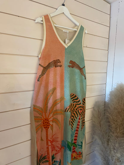 Sleeveless maxi dress with a tropical print, showcasing palm trees and leaping leopards, made from vegan materials and displayed hanging on a white wooden wall.