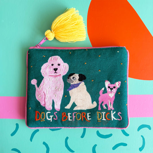 A funky dog handbag, this green velvet pouch displays embroidered images of three dogs, the phrase DOGS BEFORE DICKS, and a yellow tassel, all set against a colourful abstract background.