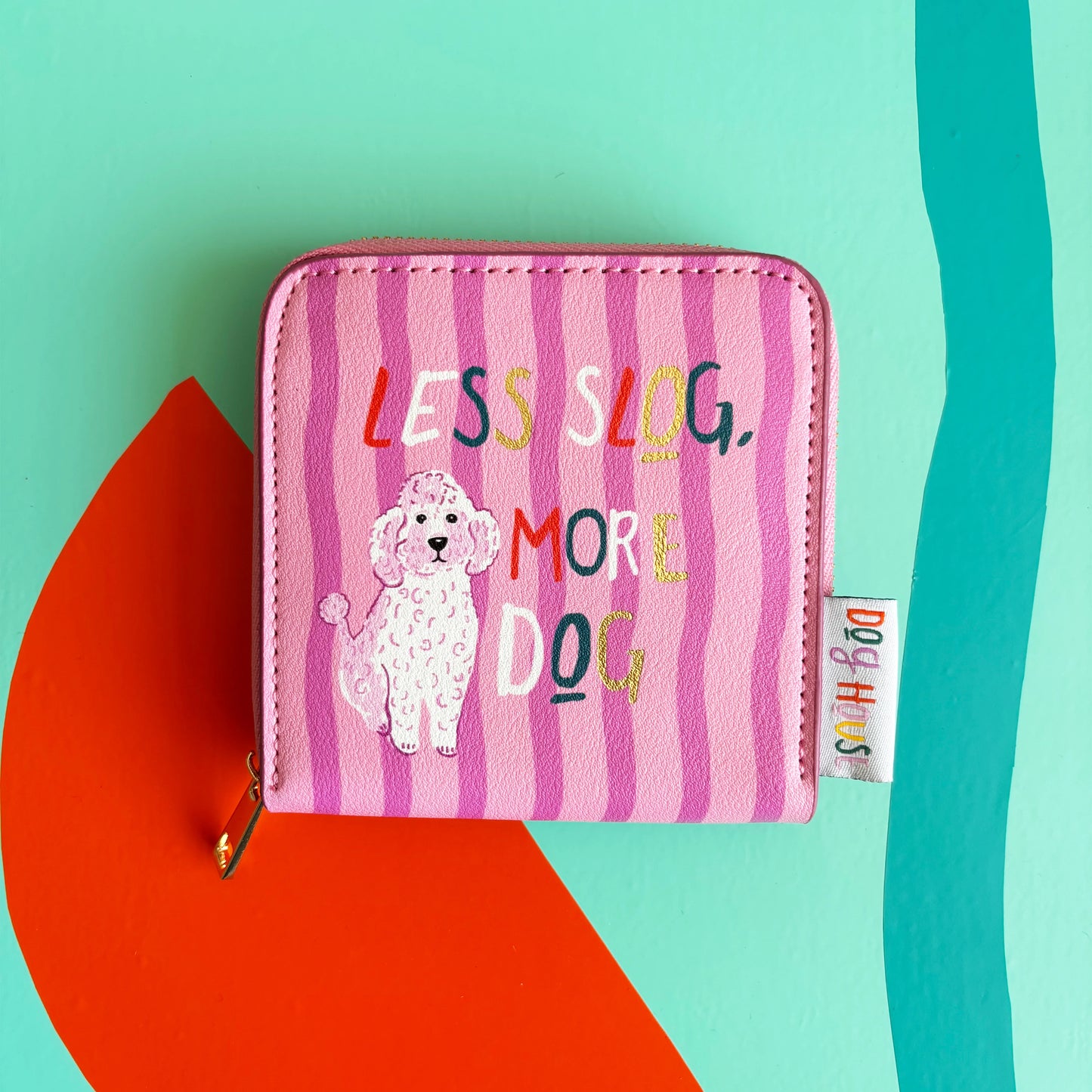 A pink zippered pouch from the Doghouse collection, featuring a cartoon poodle and the text LESS SLOG, MORE DOG on a colourful, abstract background—ideal for dog lovers.