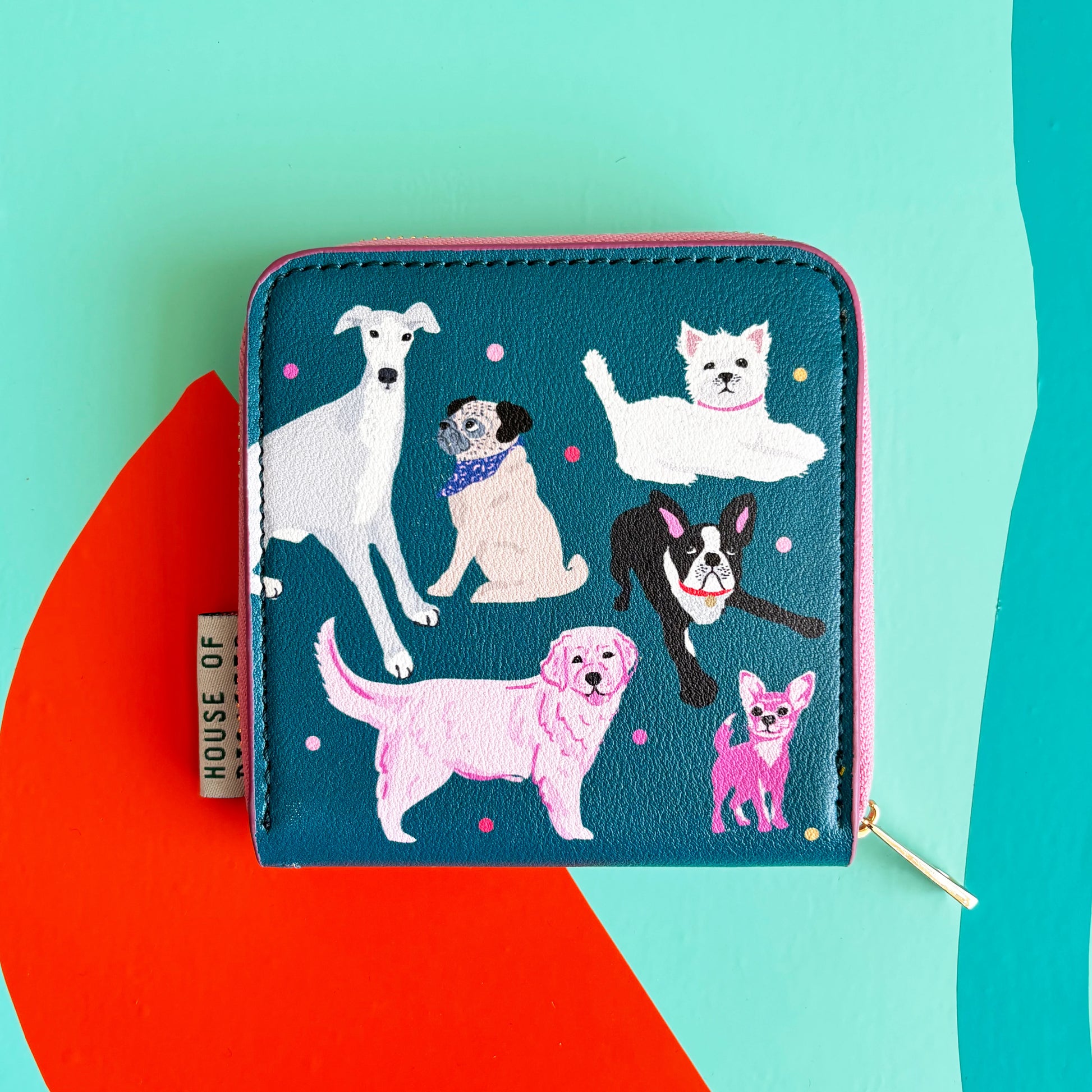 A teal zip purse from the Doghouse collection featuring six dog breeds, pink and purple dots, and a House Of tag—ideal for dog lovers. Set against a multicoloured abstract background.