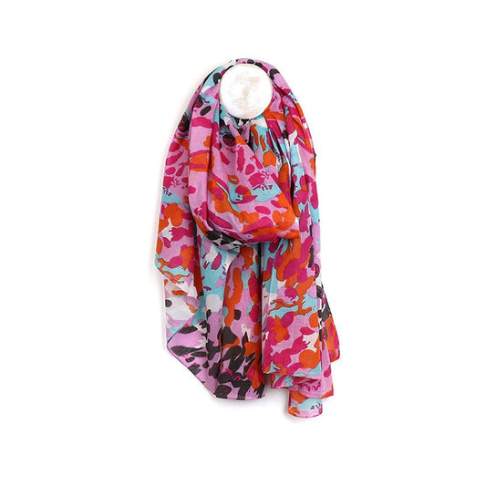A colourful, lightweight scarf crafted from vegan materials, displaying a vibrant abstract pattern in pink, red, purple, blue and orange, hanging on a wall hook.