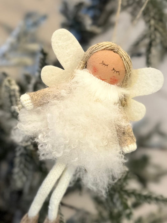 A handmade Christmas angel decoration with white wings, a fluffy white dress, and closed eyes hangs from a Christmas tree, bringing festive cheer to your holiday décor.