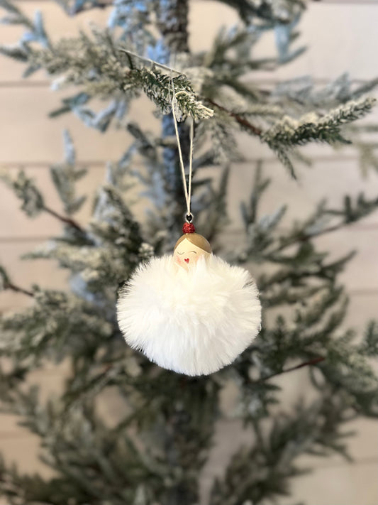 A white, fluffy bauble with a face hanging from a tree, ideal as a vegan-friendly Christmas decoration.