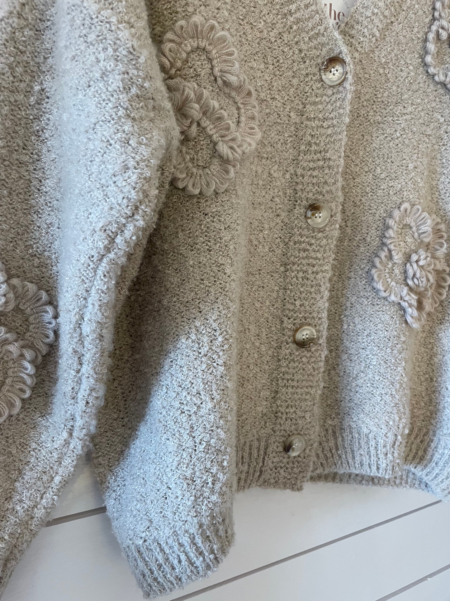 A vegan-friendly Soft Flower Cardigan in beige textured knit, adorned with large floral appliqués and five round buttons, crafted from ultra-soft fabric, shown against a white background.