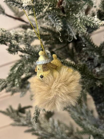 A delightful Doggy Christmas Tree Decoration showcasing a gold-coloured bear with a silver hat, clutching a fluffy tan pom-pom, hanging from a snow-dusted tree branch—perfect for festive décor and dog lovers.