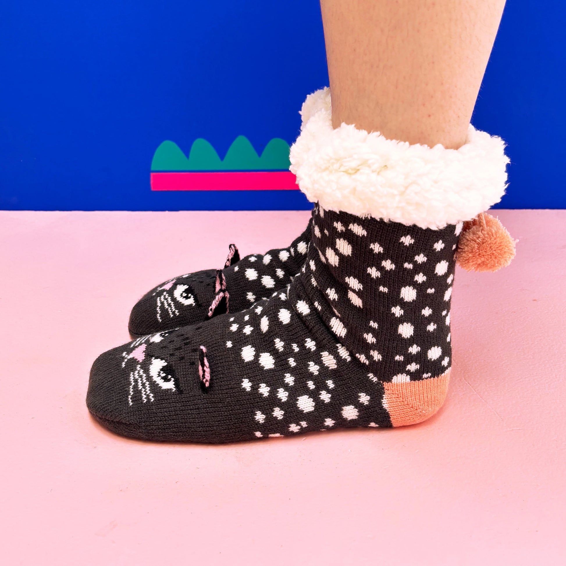 Person wearing Cat Face Slipper Socks with fluffy white cuffs, standing on a pink floor with a blue and green background—ideal anti-slip socks for any cat lover’s gift.