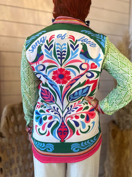 Person with short red hair wearing a funky statement shirt with floral patterns and song of faith on the back, standing indoors facing away from the camera—perfect for festival season.