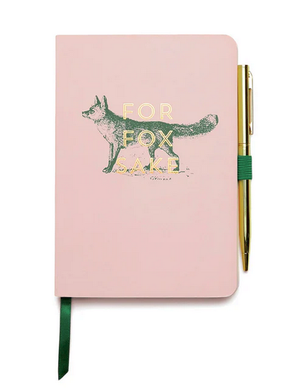 A pink hardback planner with a green fox illustration and gold “For Fox Sake” lettering, complete with ribbon markers and a pen holder containing an attached gold pen.