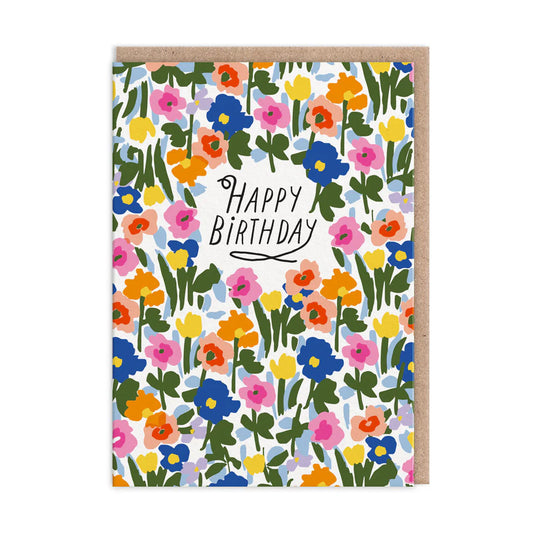Birthday card featuring a vibrant floral scene with meadow flowers in blue, pink, yellow, and orange hues. The words Happy Birthday are elegantly printed in the centre.