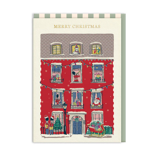 Illustration of a red townhouse adorned for Christmas, with people and pets at the windows, a sleigh on the doorstep, and carol singers outside—ideal for a festive Christmas card or holiday house card.