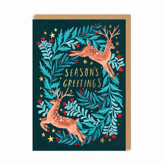 Christmas card with two illustrated reindeer, a wreath of blue-green foliage, red berries, yellow stars, and the wording Seasons Greetings—ideal for sending holiday wishes during the festive season.