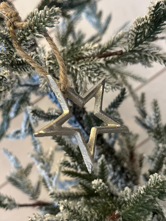 A vegan Christmas decoration, this Silver Christmas Star Tree Decoration is suspended from a snow-dusted evergreen branch, secured with twine.