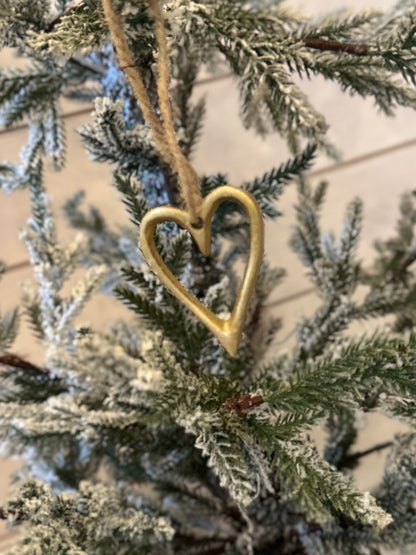 A gold, heart-shaped ornament, an ideal Christmas Heart Tree Decoration, hangs on a snow-dusted artificial pine branch—delightful vegan-friendly festive décor.