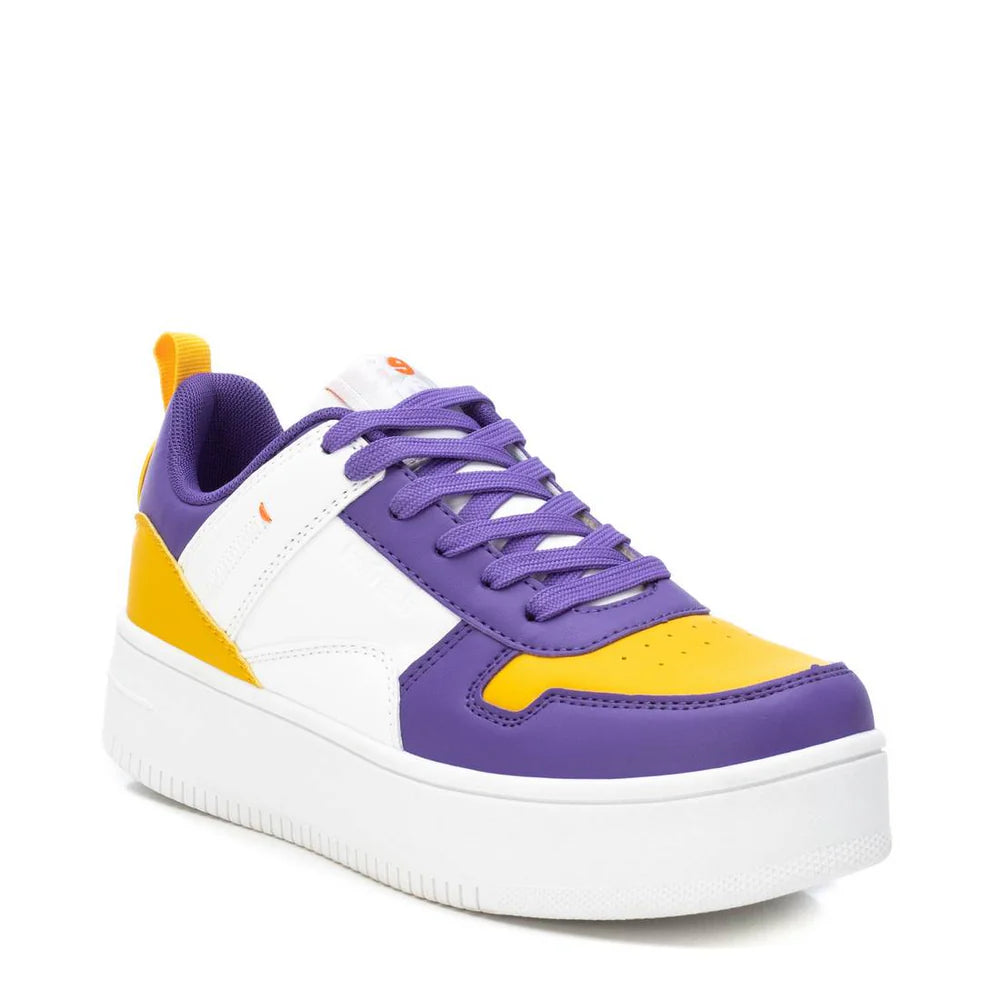 A low-top cruelty-free trainer with a chunky white sole, showcasing purple, yellow, and white panels, purple laces, and an orange pull tab at the heel.
