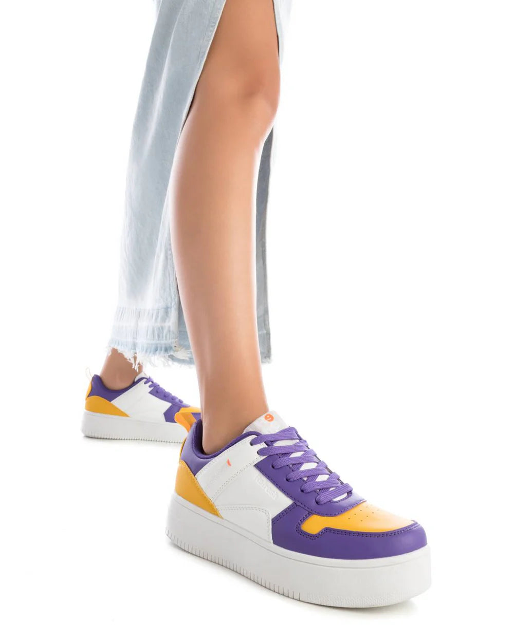 A person wearing light blue jeans and women's stylish trainers—white trainers with purple and yellow accents—is standing against a white background.