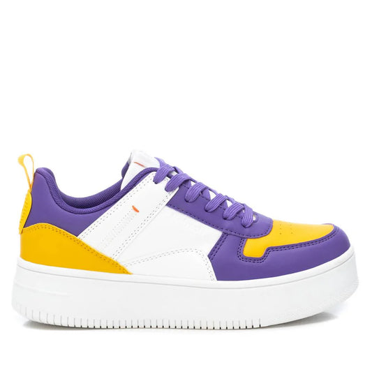 A low-top women’s stylish trainer with a chunky white sole, showcasing purple, yellow and white panels, purple laces, and a yellow pull tab at the heel—all made from cruelty-free vegan leather.