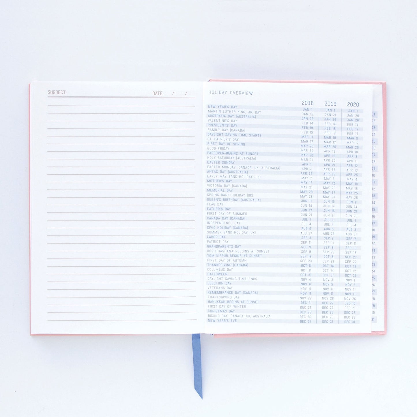 An open premium notebook with lay-flat binding, displaying a lined notes page on the left and a holiday overview for 2018 to 2020 on the right, along with a blue ribbon bookmark.