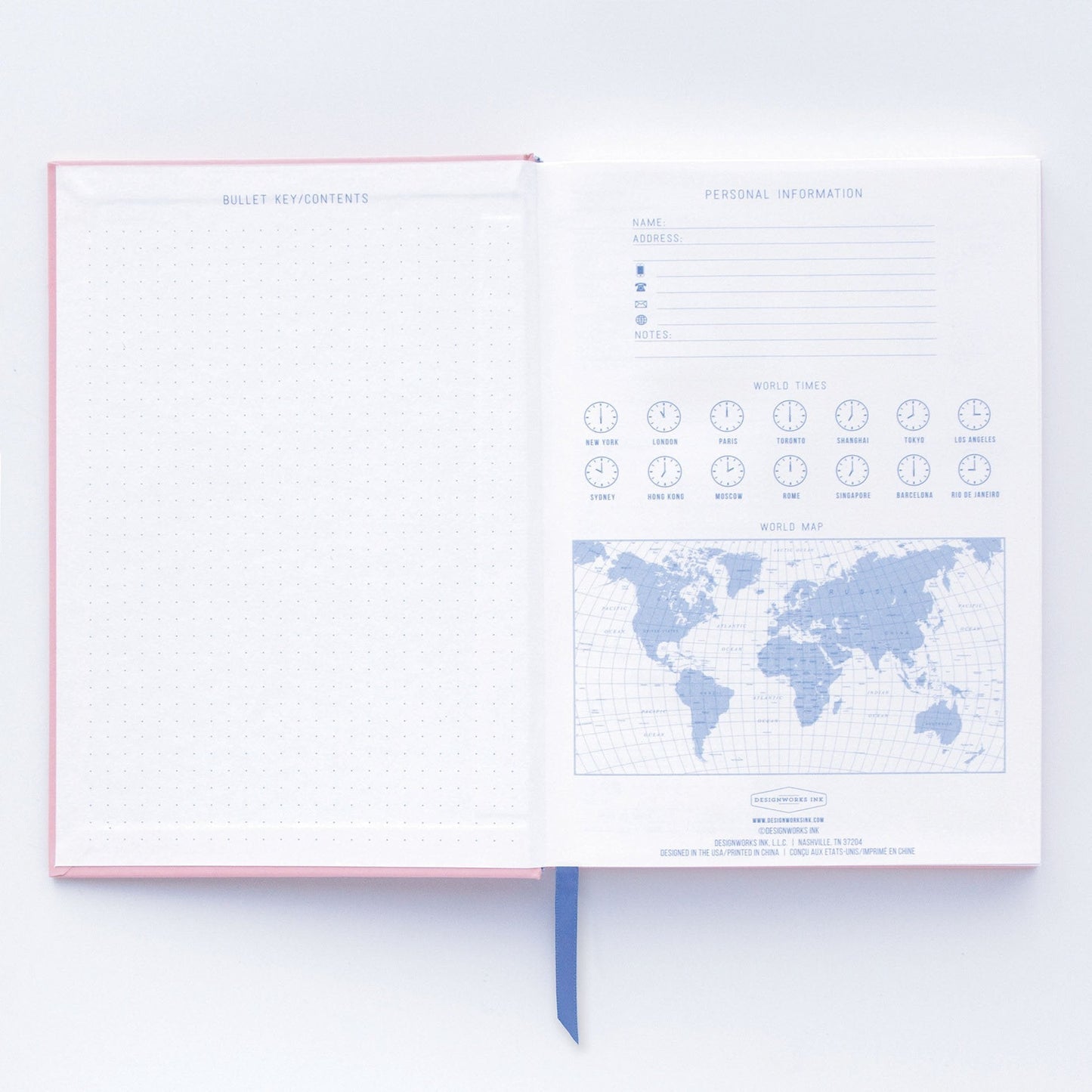 An open premium notebook with a soft-touch cover shows a dotted grid page to the left and, on the right, a personal information form, world clocks, and a world map.