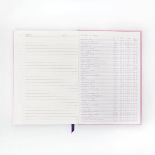An open premium notebook with lay-flat binding shows a lined notes page on the left and a holiday overview chart featuring dates from 2019 to 2022 on the right.