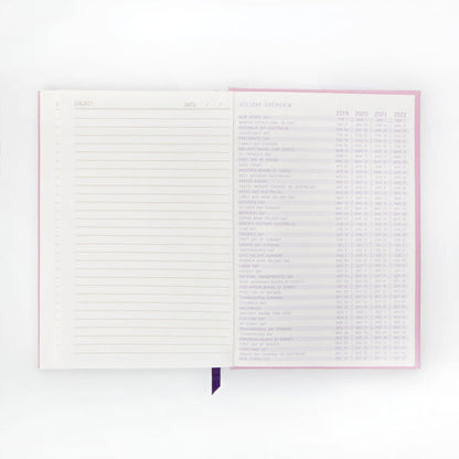 An open premium notebook with lay-flat binding shows a lined notes page on the left and a holiday overview chart featuring dates from 2019 to 2022 on the right.