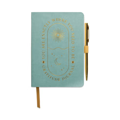 A light teal mindfulness journal featuring gold lettering and illustrations, with a matching pen clipped to the side. The cover states: You are exactly where you need to be. Gratitude journal.
