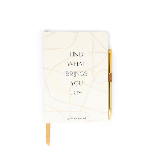 A white self-care journal with the phrase Find what brings you joy on the cover, and a gold pen attached to the right-hand side.