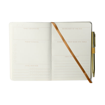 Open planner featuring sections for daily gratitude, highlights, focus, goal tracker, things that made you smile—ideal as a mindfulness journal—with space for free thoughts and a gold pen secured by a brown elastic band.