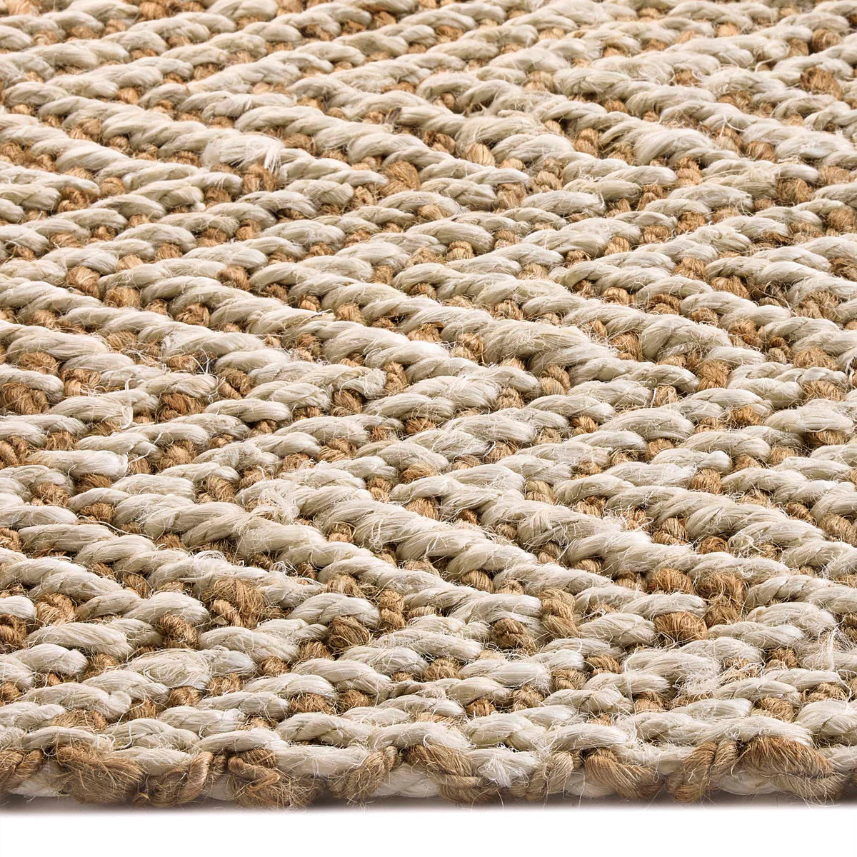 Close-up view of a handmade rug displaying a woven natural fibre design with a braided texture in light beige and tan colours.